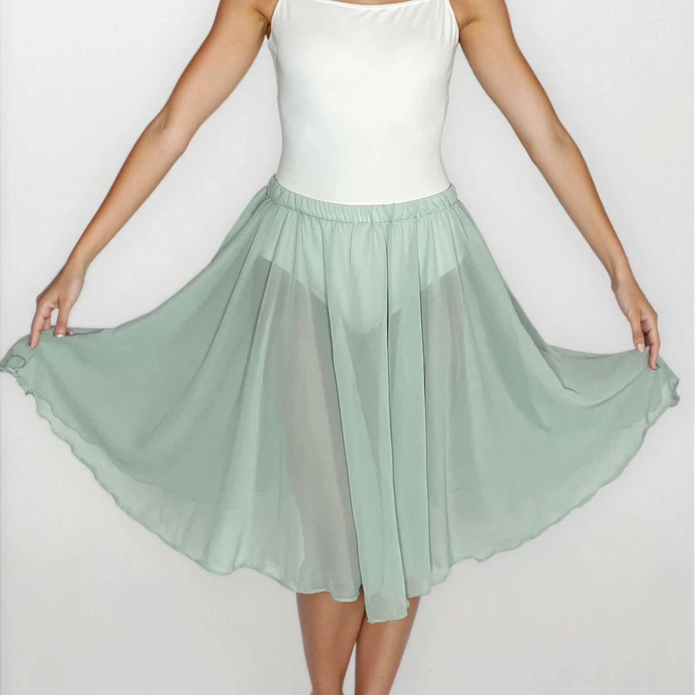 Woman wearing a white top and light green skirt on a plain background