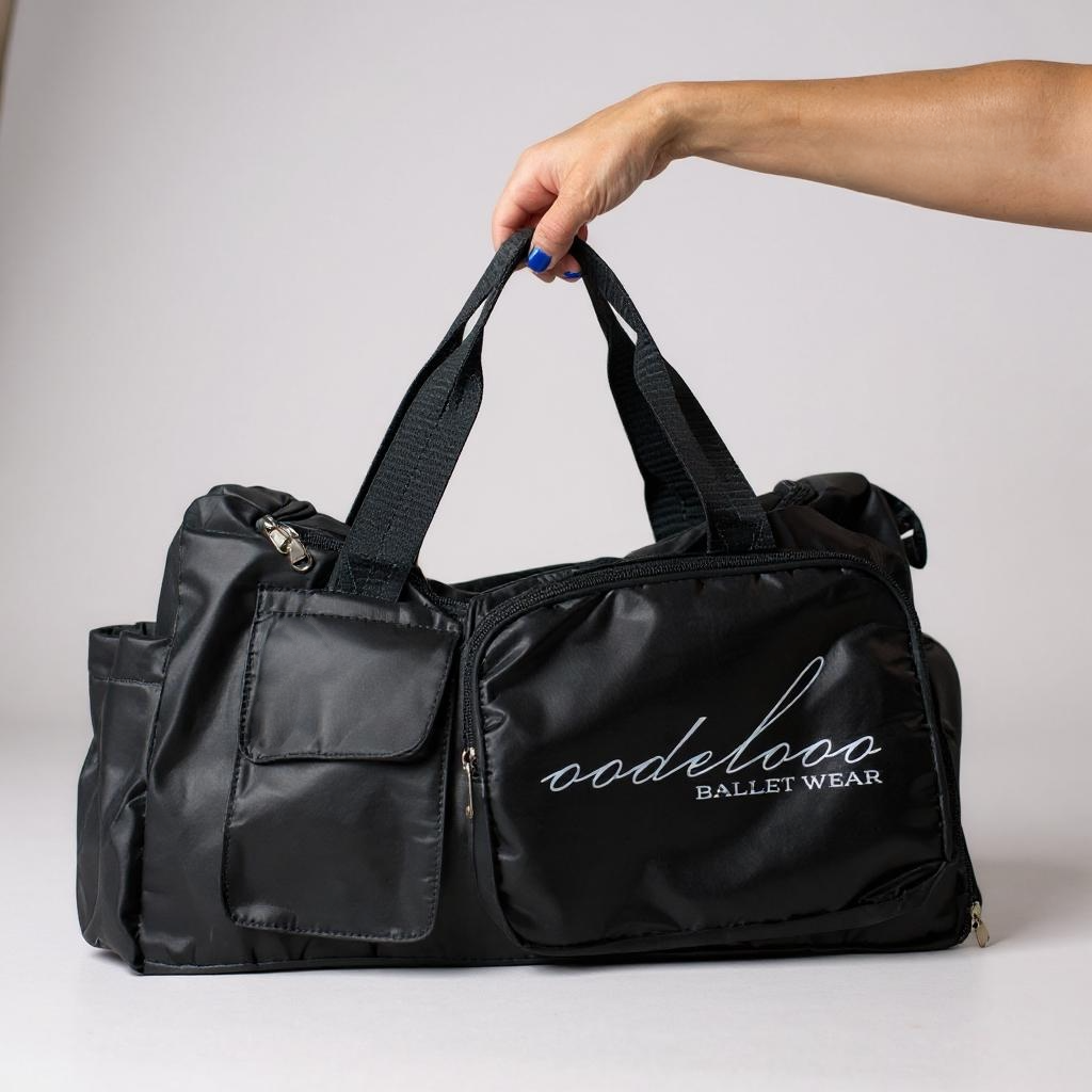 Black duffel bag with 'oodeloo Ballet Wear' logo held by a hand on a light gray background