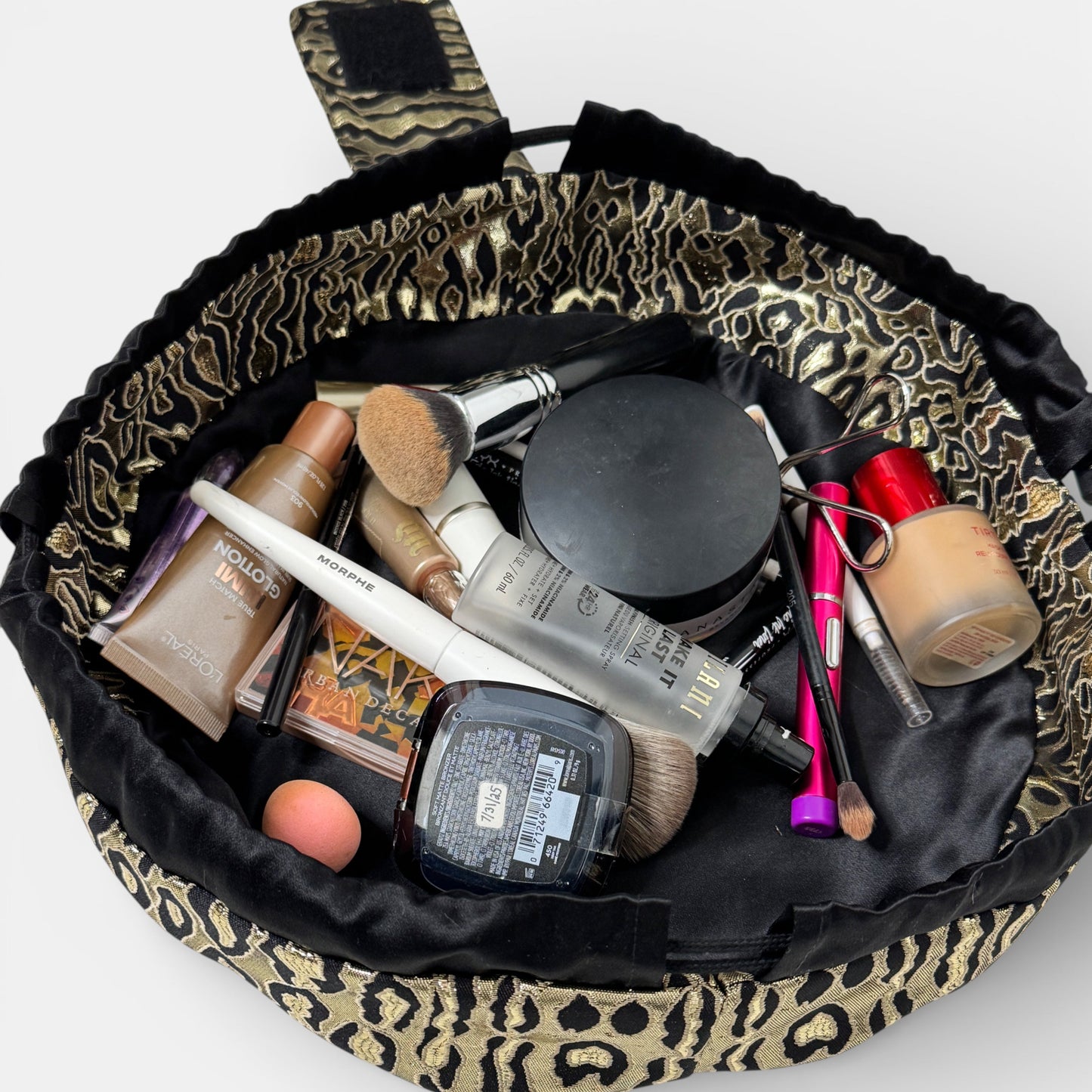 Makeup bag with leopard print trim filled with makeup items on a white background
