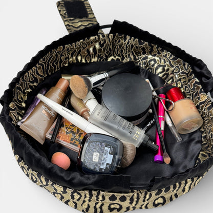 Makeup bag with leopard print trim filled with makeup items on a white background