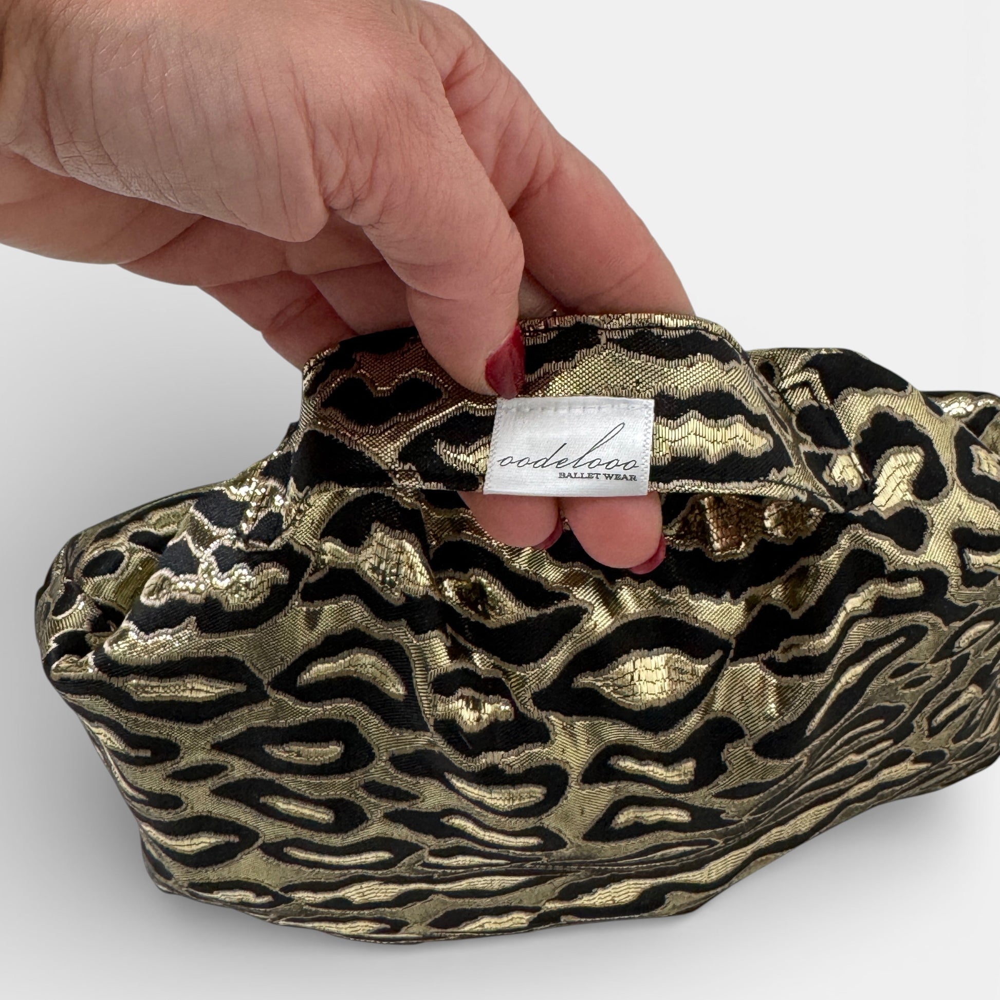 Hand holding a gold and black patterned handbag with a visible brand label on a white background