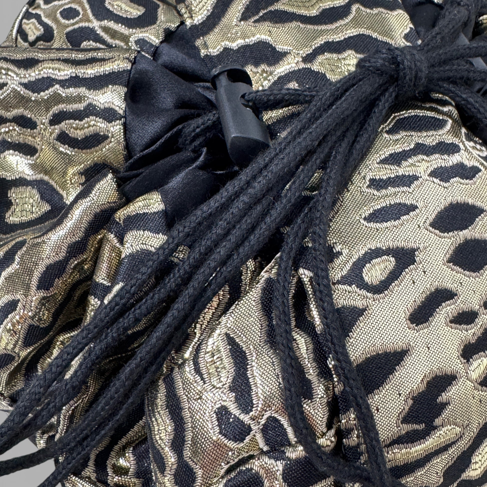 Gold and black patterned fabric with black drawstrings on a gray background