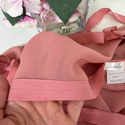 Close-up of pink fabric with a visible brand label held by a hand, with flowers in the background.