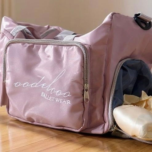 Pink bag with 'oodelooo Ballet Wear' branding on a wooden floor.