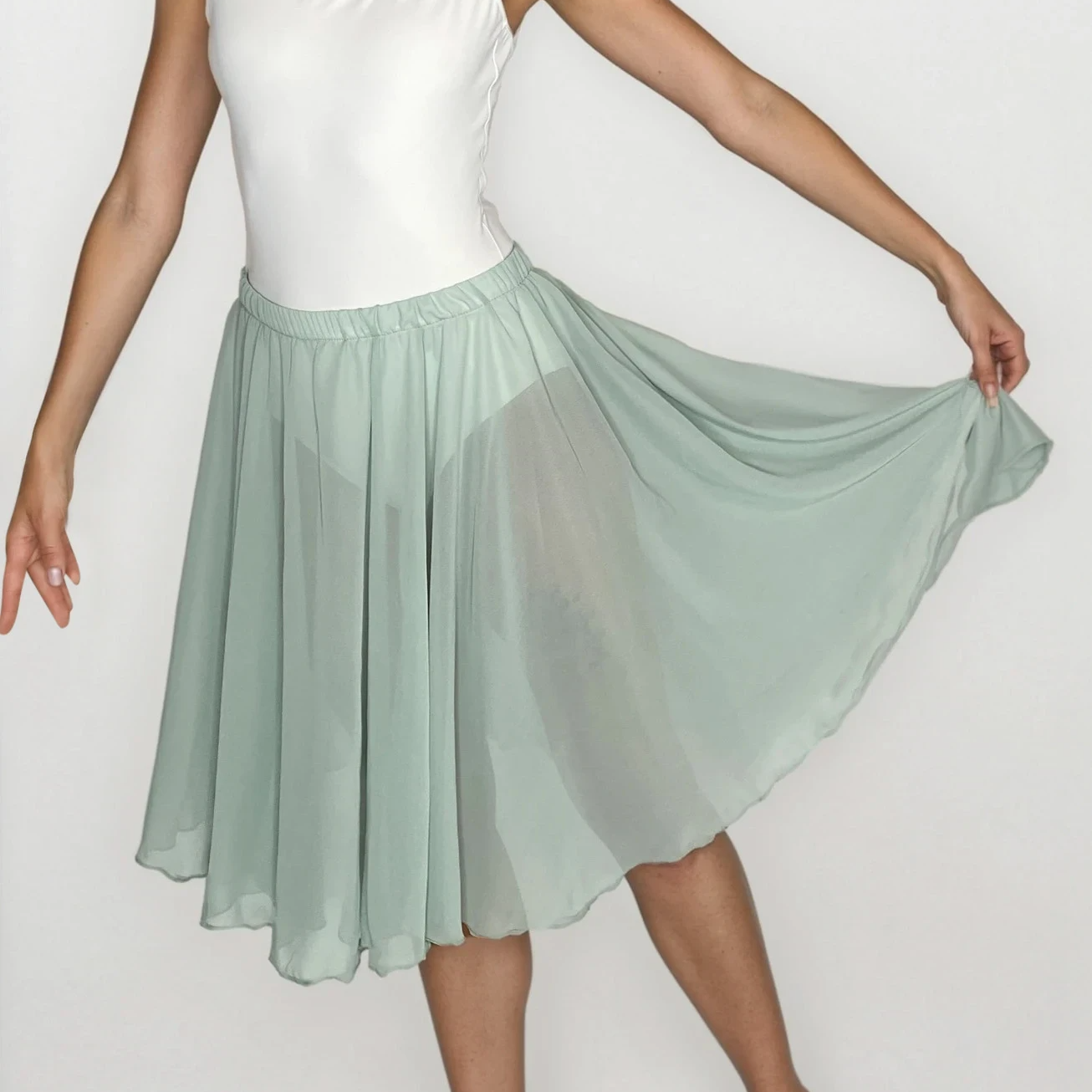 Woman wearing a white top and light green skirt on a plain background