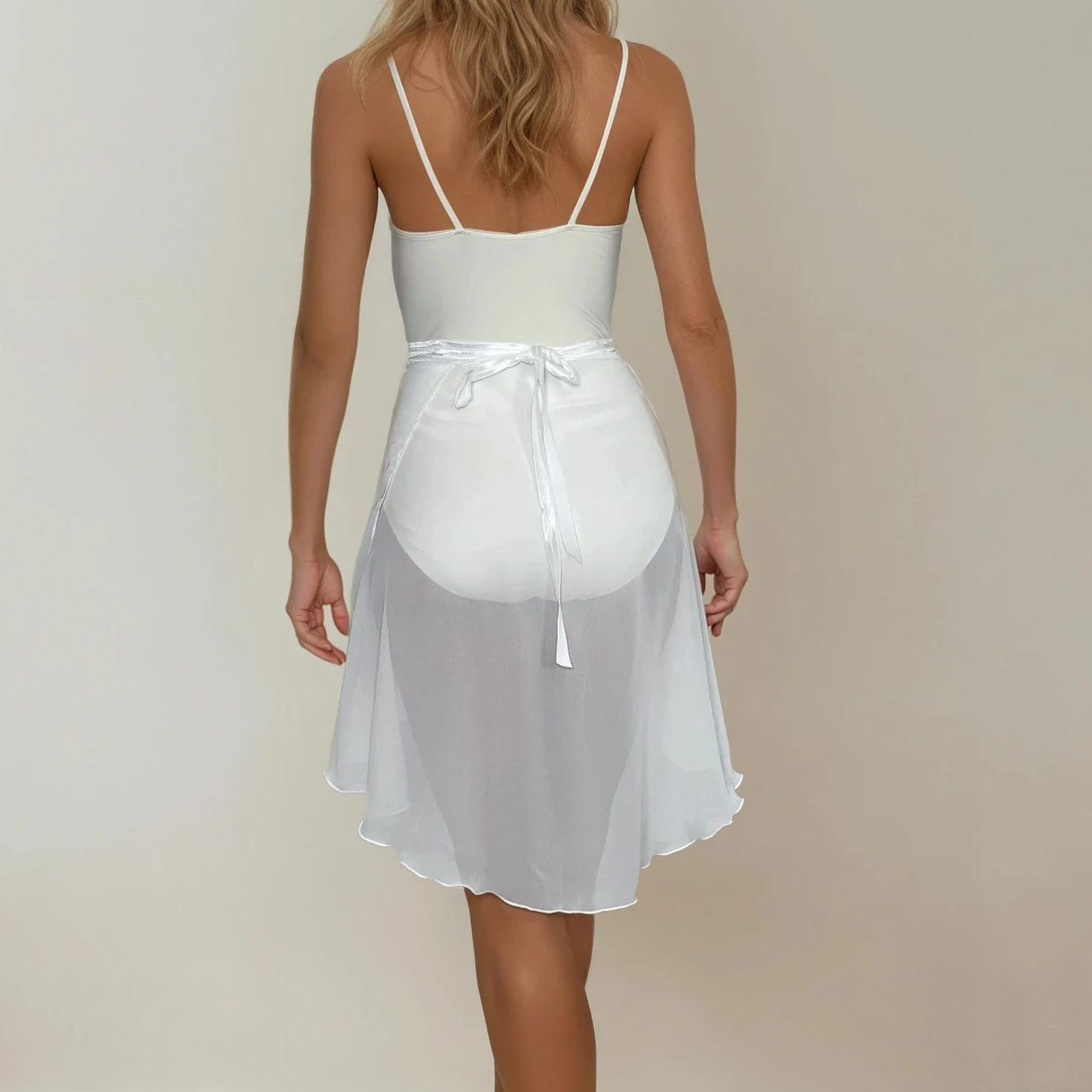 Woman wearing a white dress with sheer overlay against a plain background
